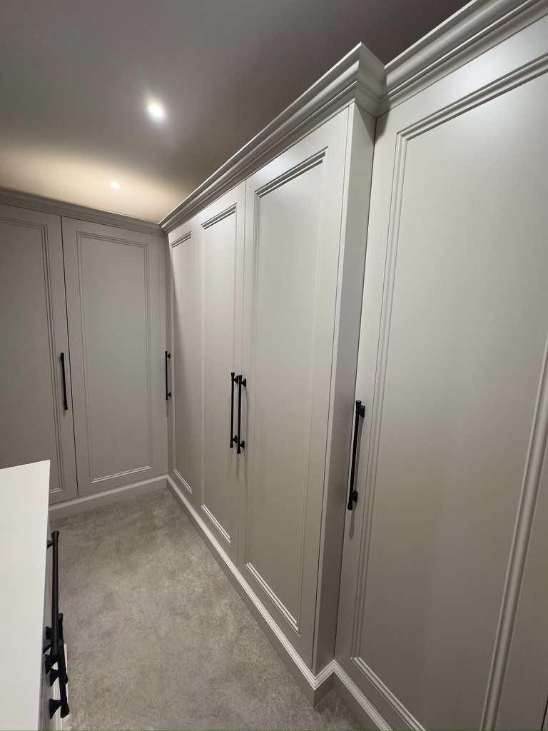 Walk-in dressing room with full-wall fitted wardrobes, crown moulding, and black handles