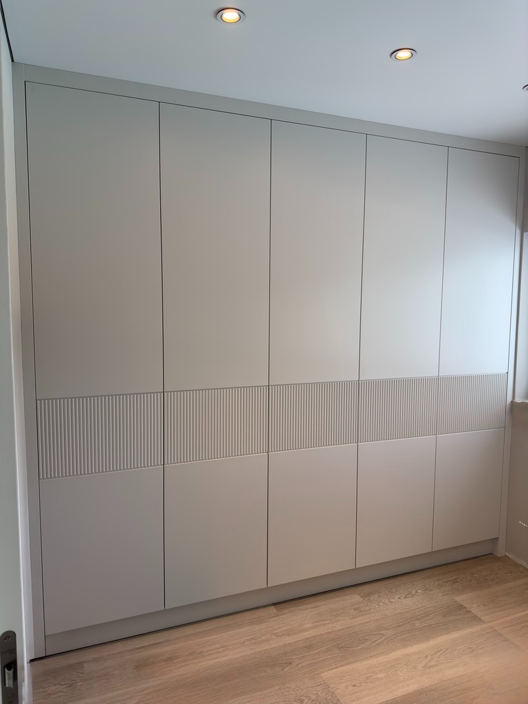 Contemporary handleless wardrobes with fluted panel detail on oak flooring