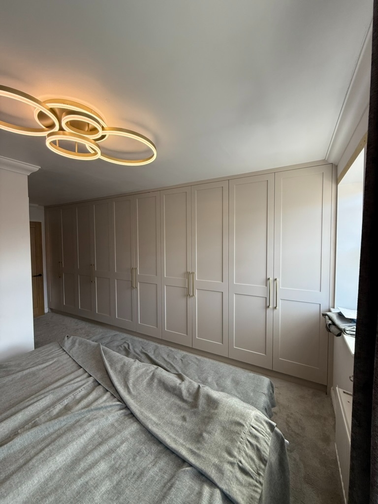 Bespoke fitted wardrobes in warm grey with brass handles — full-wall bedroom installation