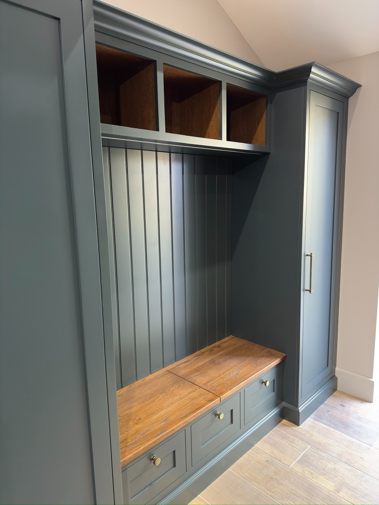Dark green boot room with oak cubbies, tongue-and-groove panelling, and brass hardware — angle view
