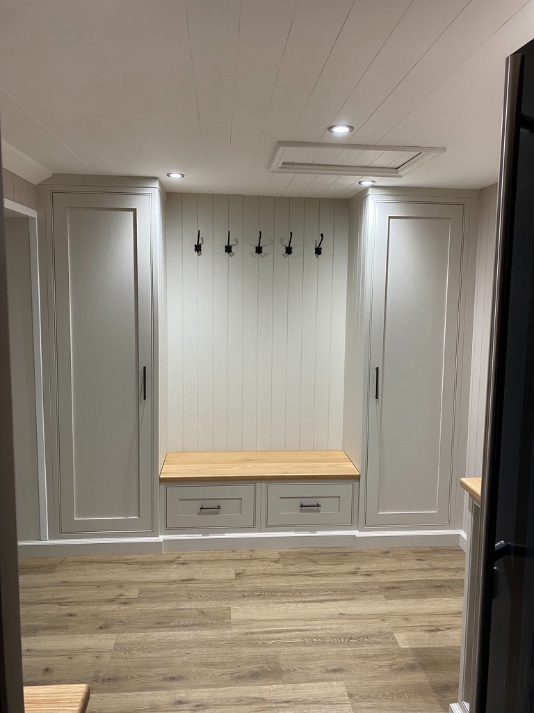 Light grey boot room with full-height wardrobes, bench seat, coat hooks, and oak worktop