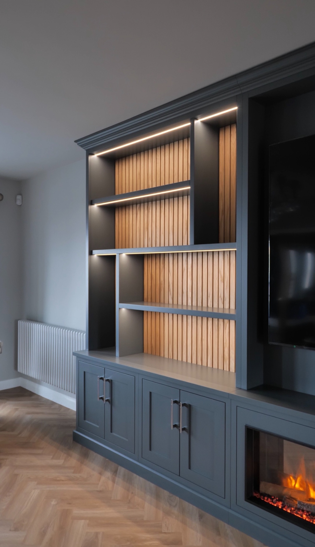 Bespoke media wall with oak slatted backing, LED lighting, and integrated fireplace — fitted furniture East Yorkshire
