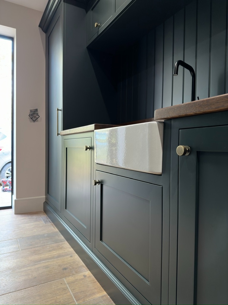 The Stables — close-up of Belfast sink with dark green shaker cabinetry and brass hardware